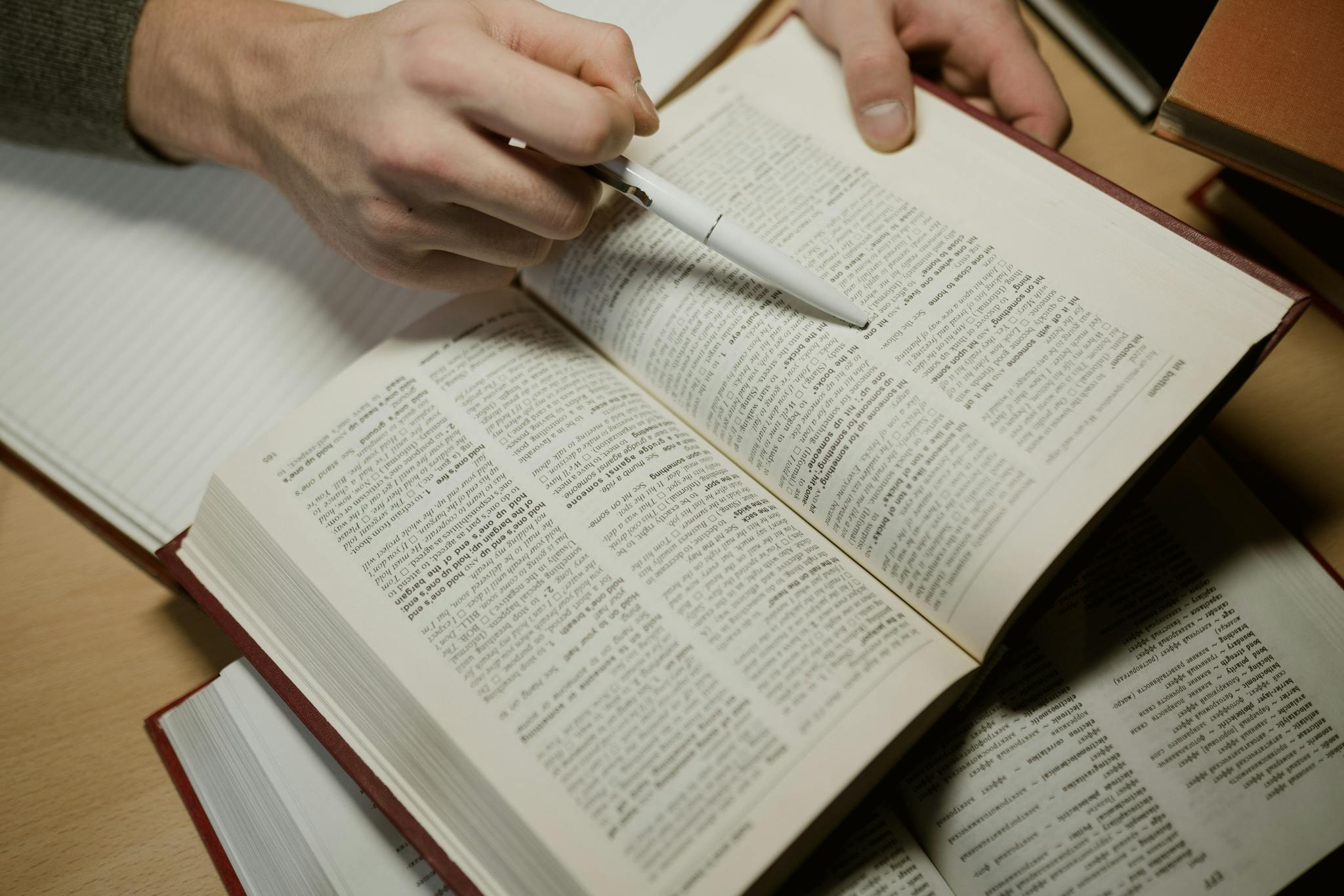 A hand holding a pen while studying an open book, highlighting learning and education.