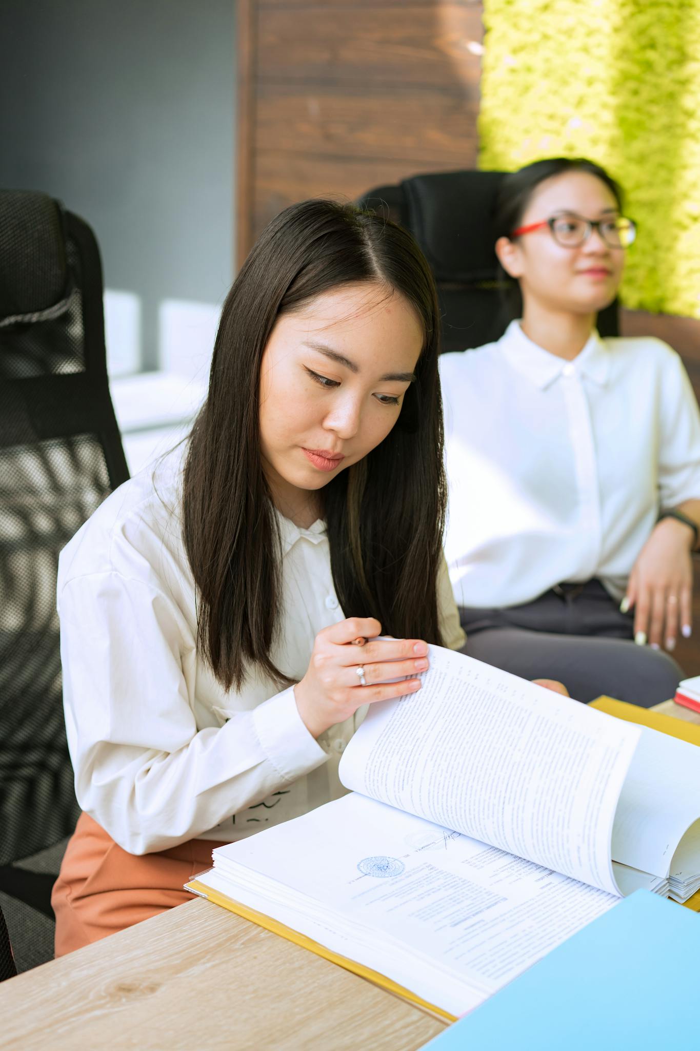 Two professional women reviewing documents in a modern office setting.